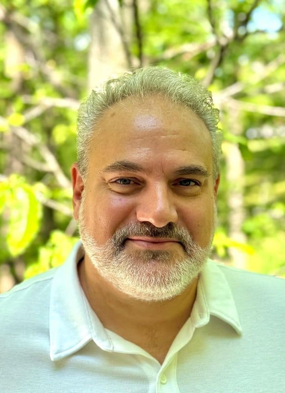 Headshot of a man with graying hair and beard, wearing a white polo shirt.