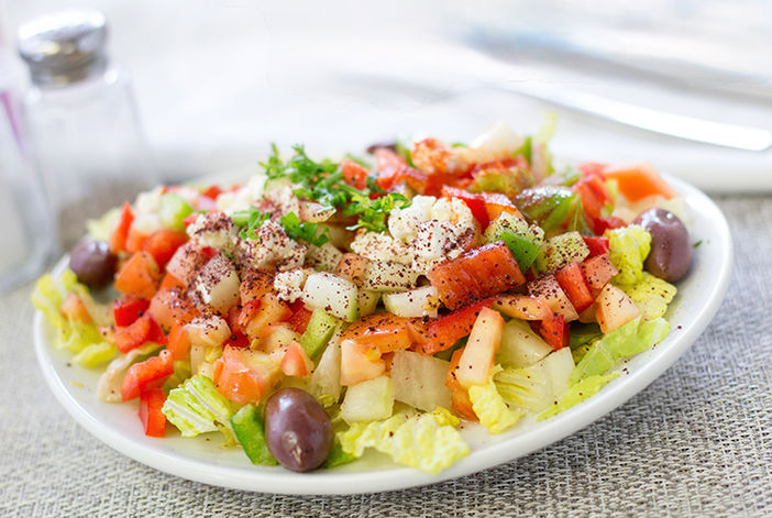 Vibrant fresh salad with tomatoes, cucumbers, olives, lettuce, and seasoning.