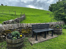 Bench in Grindelton against a stone wall, surrounded by flowers and fields