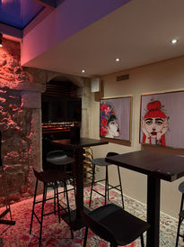 Bar-Interieur mit Tischen, Stühlen und Kunstwerken an der Wand.