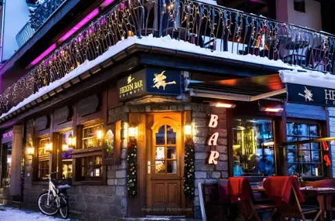 Dimly lit bar with red chairs, low tables, and wooden beams on the ceiling, creating a mysterious and stylish vibe.