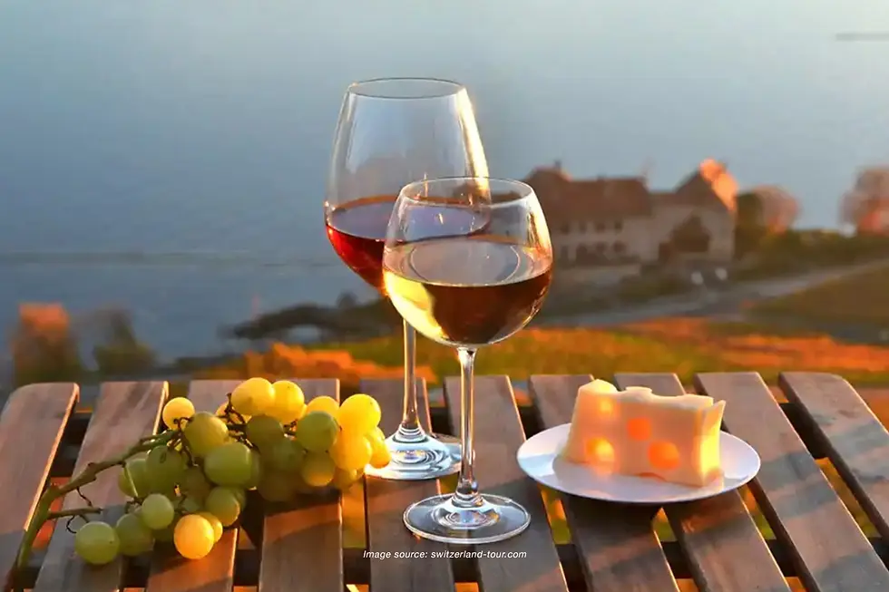 Two wine glasses with grapes and cheese on a wooden table overlooking Swiss Vineyards and a calm lake during a golden sunset.