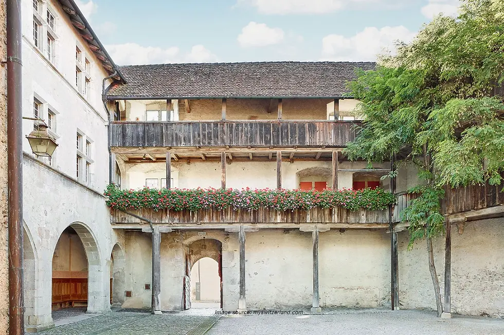 Château de Crayes with i-k historic courtyard, wooden balconies, flower boxes, and stone arches that reflect the charm of Swiss heritage.