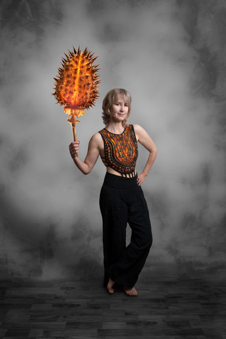 Une femme pose avec un flambeau dans une main en forme de graine de datura illuminé sur fond gris