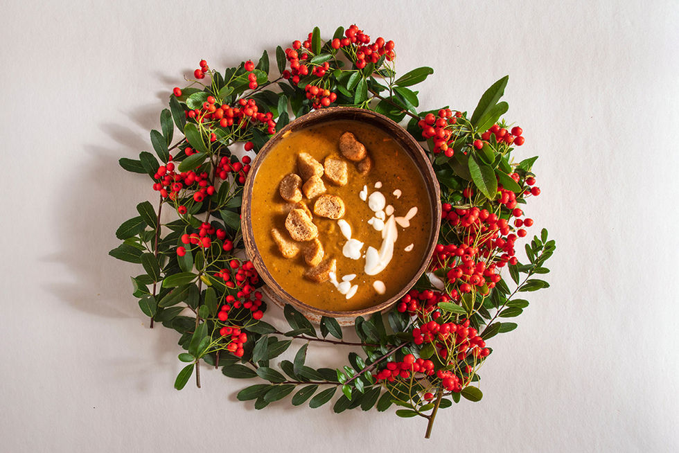 Un bol de soupe orange avec des croutons de pain entouré de branche de baies rouges comme une couronne de Noel