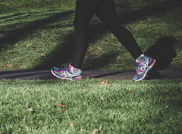 A woman walking briskly through a park in jogging shoes and yoga pants. Zone 2 exercise.