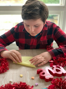 boy making origami hearts valentines card decoration on table