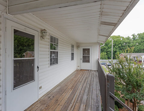 The Manor Townhomes rear image. Wood patio, door and windows. Trees over the patio. 