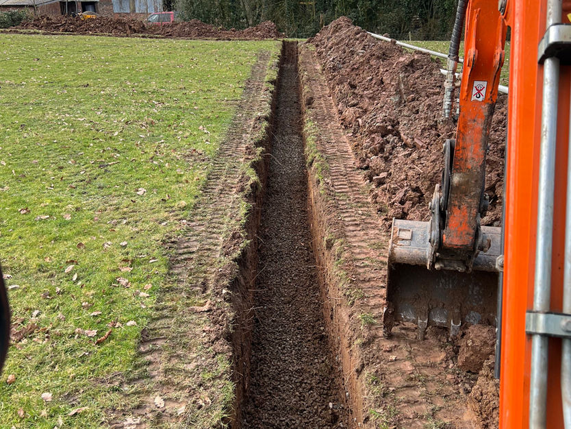 Reilly Groundworks mini digger excavation for drainage installation in a field.