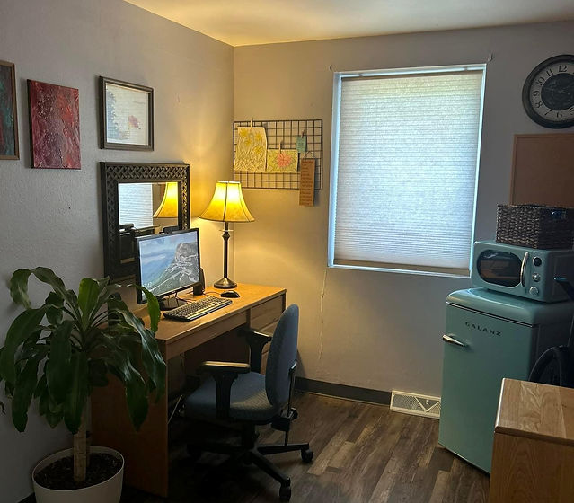 Interior of the Amity Treatment facility. The image shows a tele-health room that has a desk, computer chair, and computer with a web cam for conferencing.