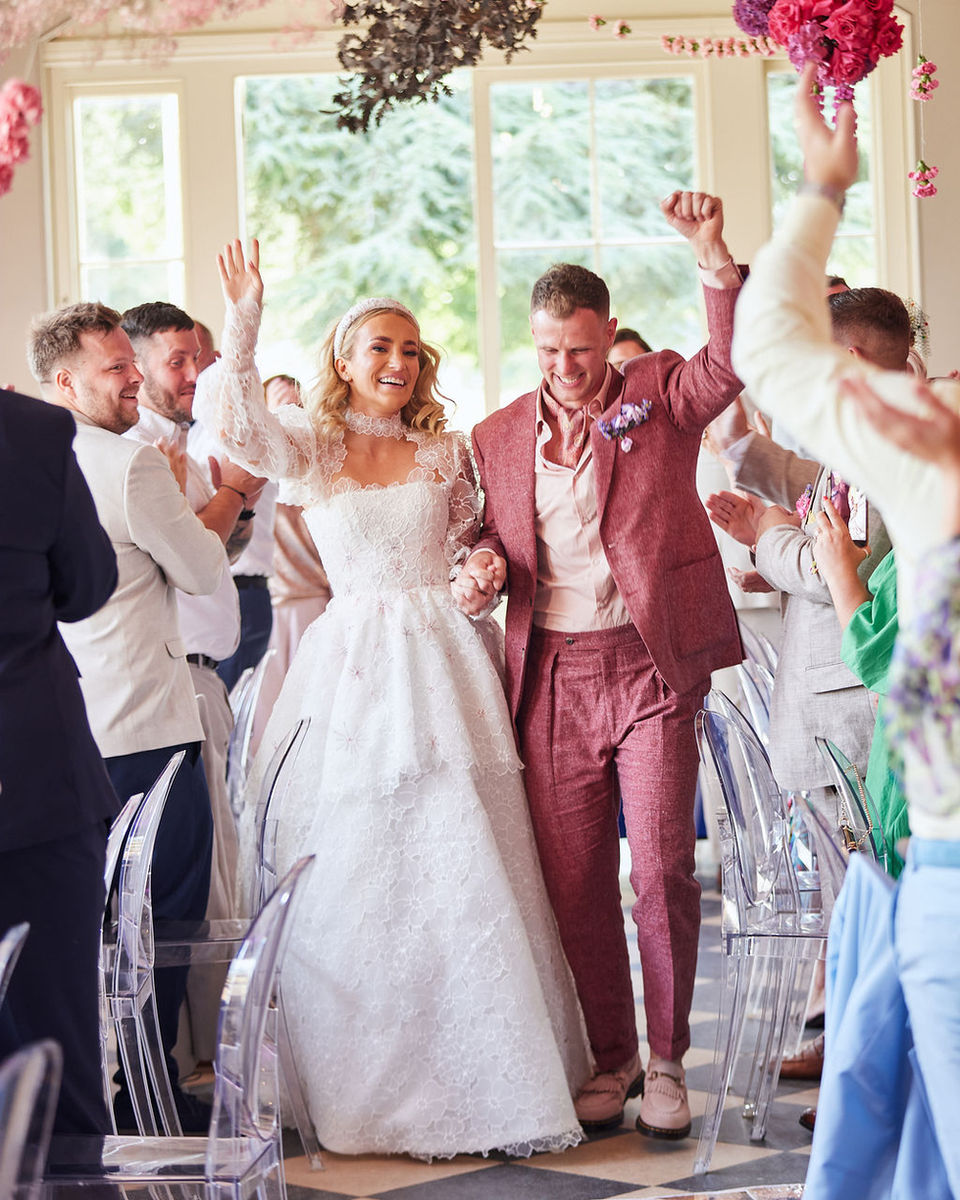 Bride and groom enter their wedding breakfast room, while their guests stand and cheer.