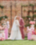 Bride and groom kissing at their wedding ceremony, surrounded by lush modern florals in pink hues