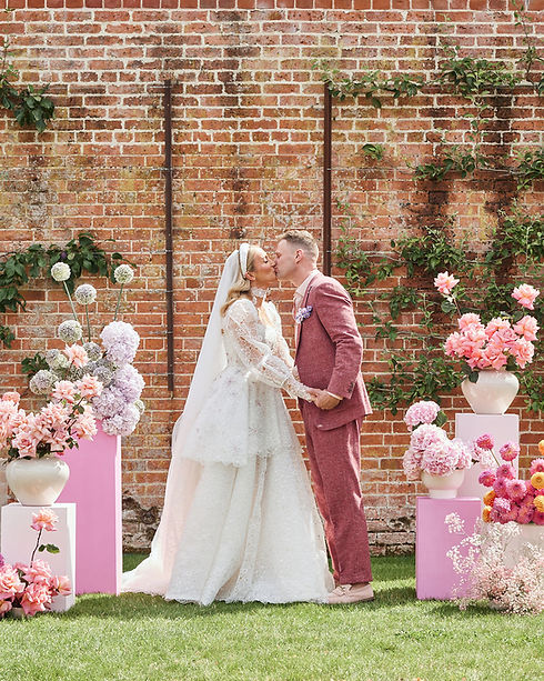 Bride and groom kissing at their wedding ceremony, surrounded by lush modern florals in pink hues