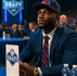 Joven jugador de fútbol americano sentado en la mesa de espera del draft, con expresión enfocada, esperando ser seleccionado. Estilo hiperrealista inspirado en videojuegos NCAA Football, ideal para contenido sobre el Draft de la NFL.