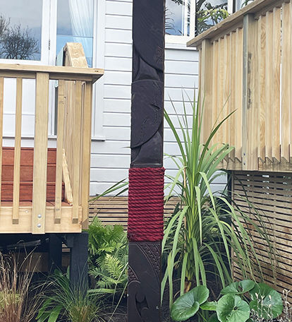 Maori carved totem pole called pou te whenua, pou of the family; bound with red rope and pictured in situ at the home of the buyer; maori sculpture art; maori commission art.