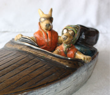 Cast bronze, coloured sculpture of two dogs in a speedboat. Cropped image.