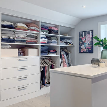 Venstre vegg under skråtak med åpne hyller, heng og bred skuffeseksjon ved siden av øyen.