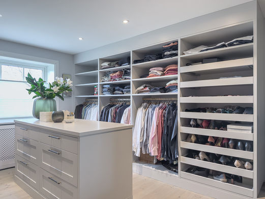 Høyre vegg i walk‑in closet med åpne hyller, heng og uttrekkbare skohyller, sett bak øyen.