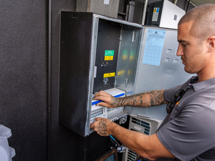 Commercial electrician working on wiring inside an external electrical distribution panel.