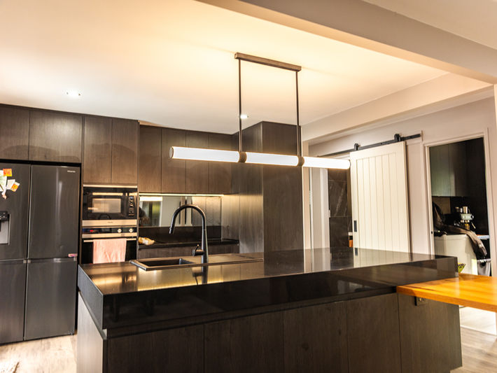 Sleek, dark kitchen with a long island bench and linear LED pendant lighting.