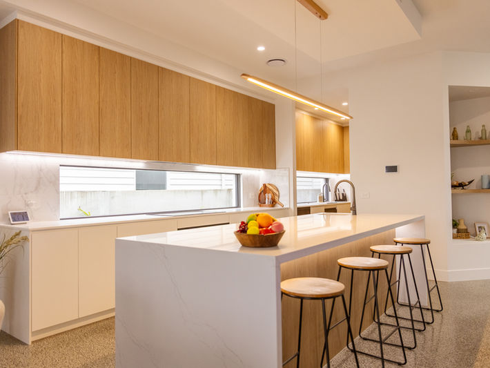 Modern kitchen with light timber cabinetry, white island bench, and recessed lighting.