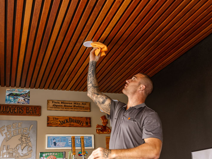 Electrician installing recessed downlights in a timber-slatted ceiling of a bar area.