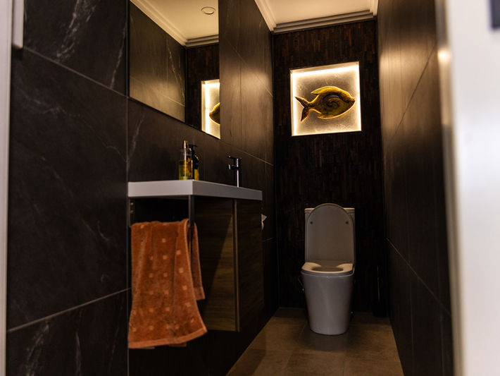 Luxury bathroom featuring accent lighting, black tiles, and a unique basin.