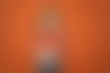 A young girl with pigtails stands against an orange background, deeply engaged in reading a red book.