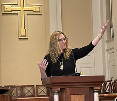 aime Clark-Soles, smiling, is teaching from behind a dais with a microphone in front of her, in a lecture setting where the audience is not visible.