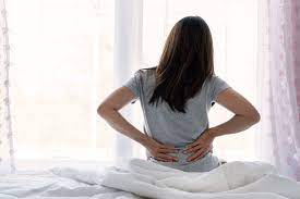 A woman sitting up from bed, holding her back.