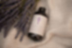 A bottle of Yorkshire Lavender Bubble Bath on a cream coloured blanket next to a bunch of dried lavender. 