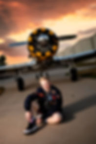 senior boy sitting in front of airplane with a propeller, with a beautiful sunset behind him