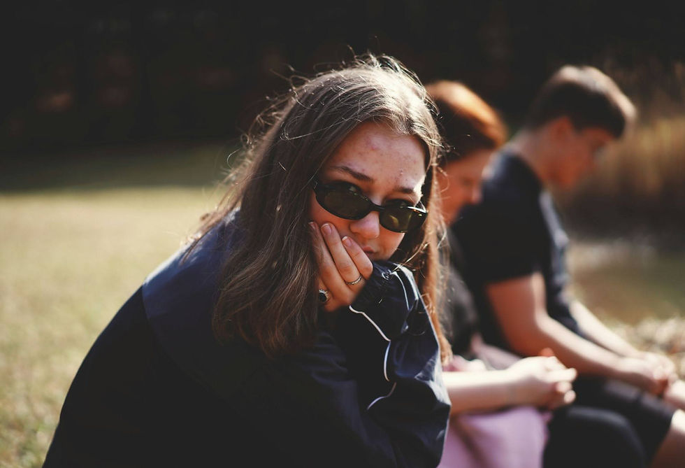 Woman sitting apart from others, appearing withdrawn and upset, illustrating emotional distress associated with ADHD rejection sensitivity dysphoria (RSD) and anxious attachment.