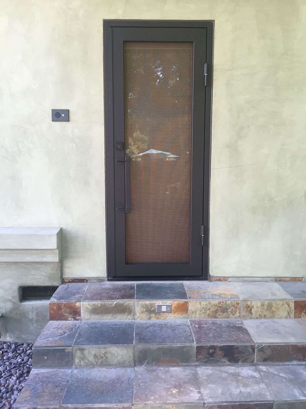 The Frame steel security screen door with a oil rubbed bronze texture above stone entry steps