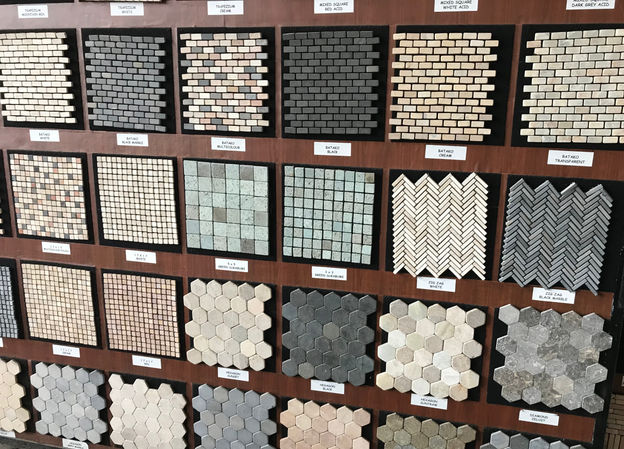Showroom display of mosaic tile sheets including hexagon, brick, and herringbone stone patterns for flooring and wall applications.