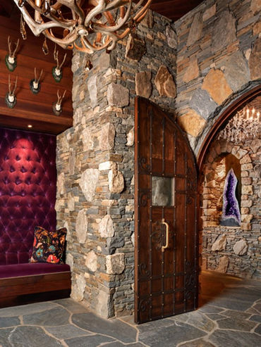 Custom wood and stone entry with carved teak doors and tufted seating in a luxury lodge or resort lobby.
