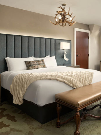 Hotel bedroom interior with custom wood furniture, upholstered headboard, bedside tables, and bench designed for luxury hospitality spaces.