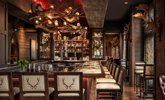 Luxury hotel bar with custom carved wood cabinetry, stone counter, and upholstered stools.