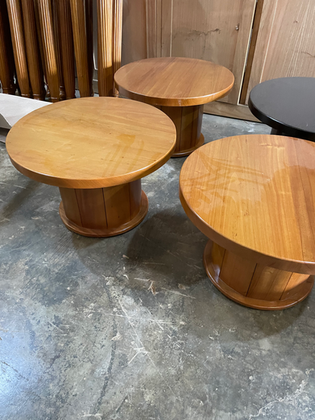 Three round solid-wood pedestal tables in natural finishes displayed in a furniture workshop.
