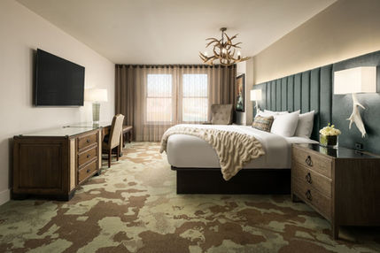 Spacious hotel room with a custom bed, upholstered headboard, dresser, and writing desk.