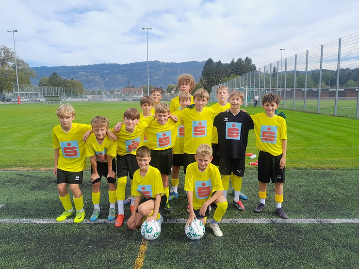 Fußballjugend in gelben Trikots mit Sparkassen-Logo auf Sportplatz in Vorarlberg