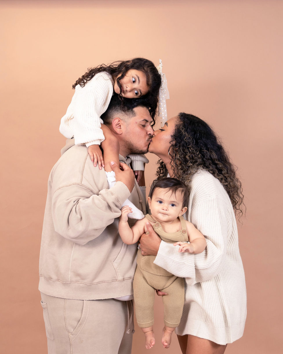 Happy family of four posing together in a bright studio setting, photographed by Osondu Digital, Central Valley family portrait photographer.
