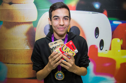Participante sorri para a foto segurando medalha e cópia do UNO