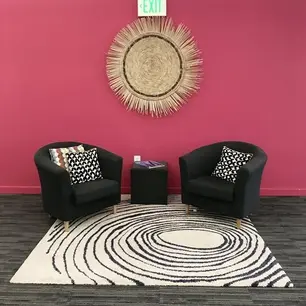 Two chairs, pink wall, circular rug, decorative piece.
