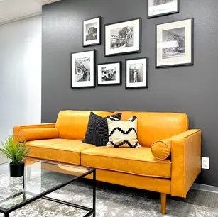 Yellow couch with pillows, framed photos on gray wall.