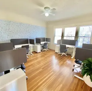 Modern office space with multiple workstations and wooden flooring.