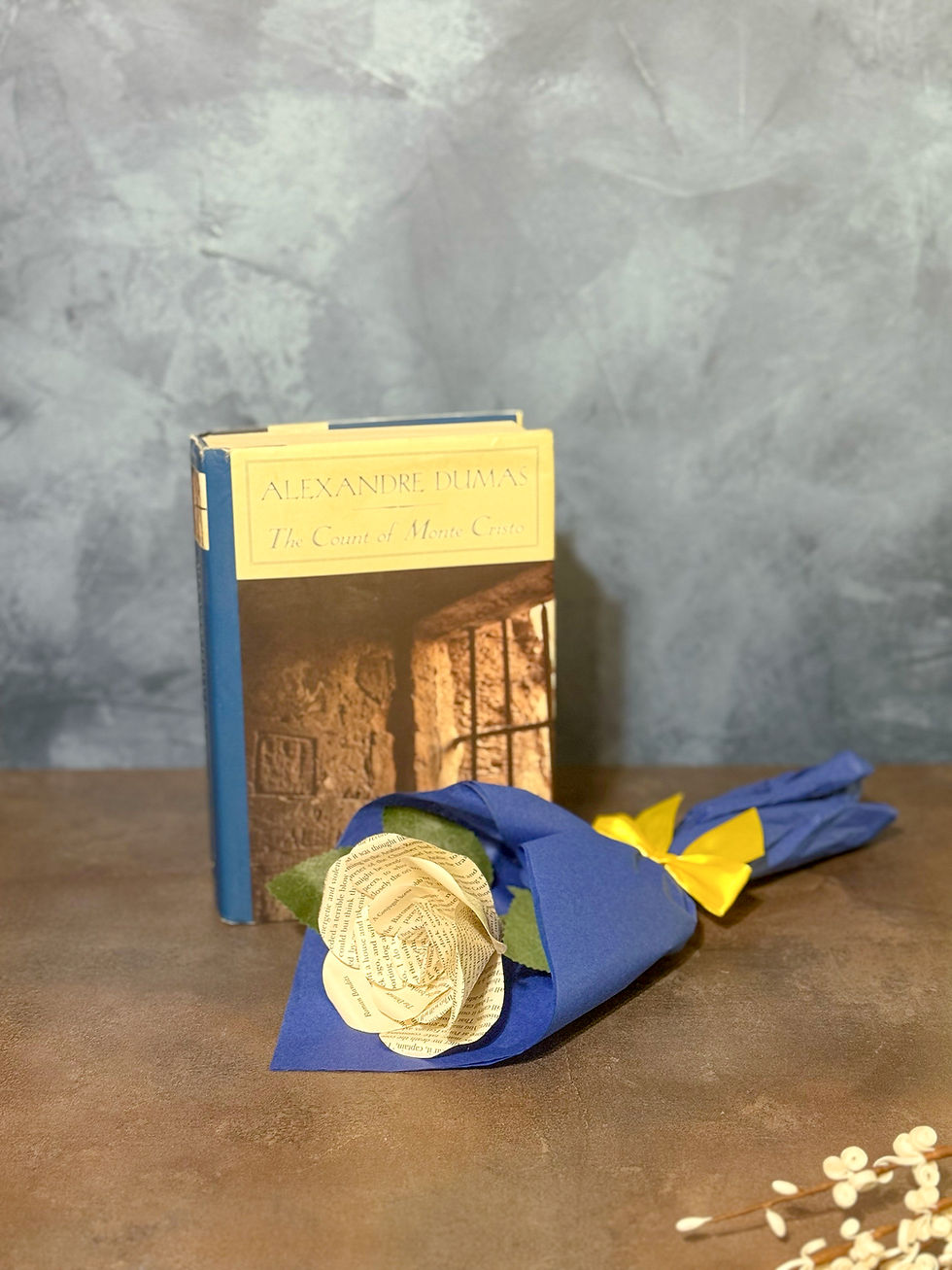 Thumbnail: Small handmade Count of Monte Cristo paper rose wrapped in blue tissue paper with a yellow ribbon, displayed beside the book.