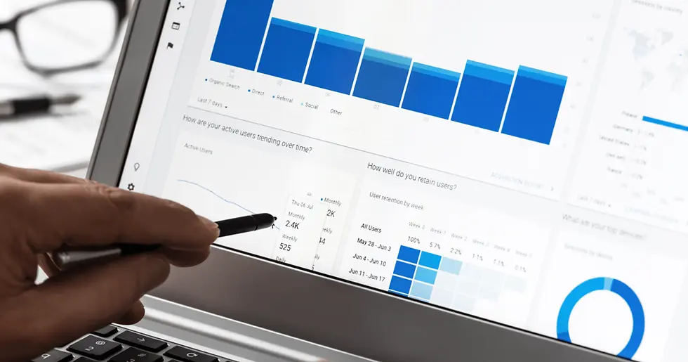 Person holding a stylus pointing at a laptop displaying analytics with blue charts and graphs, suggesting analysis or data review.