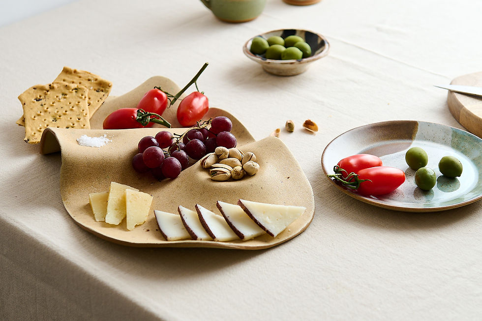 Lifestyle product photography for makers featuring a ceramic charcuterie plate styled with grapes, nuts, cheese, tomatoes and olives in a natural light setting.