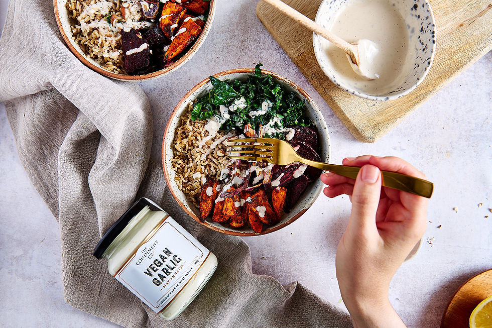 An overhead shot of a colourful veggie bowl with a jar of vegan garlic mayo next to the bow.
